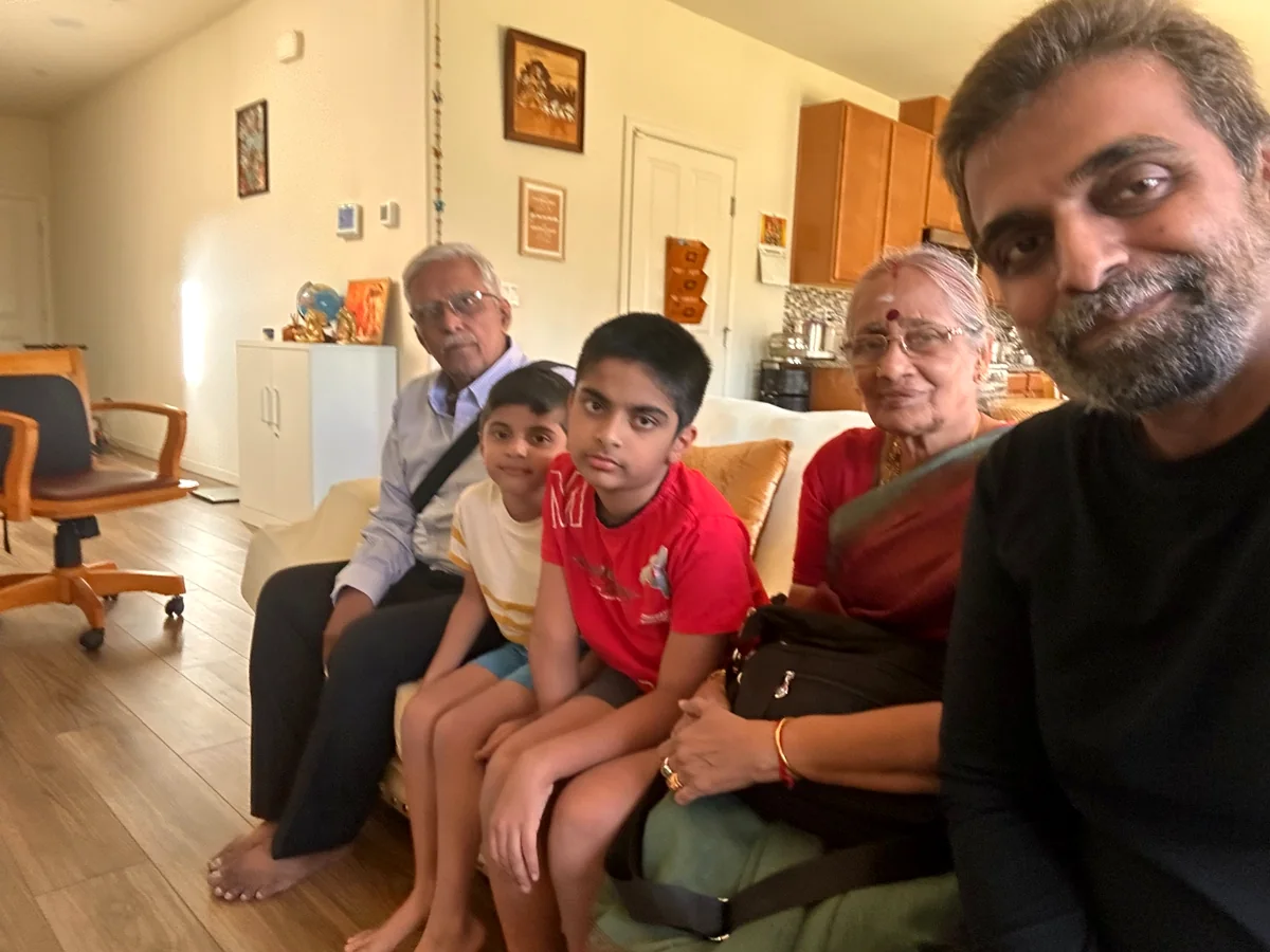 Three generations together on a sofa at home — grandparents, the two boys and Bhargav