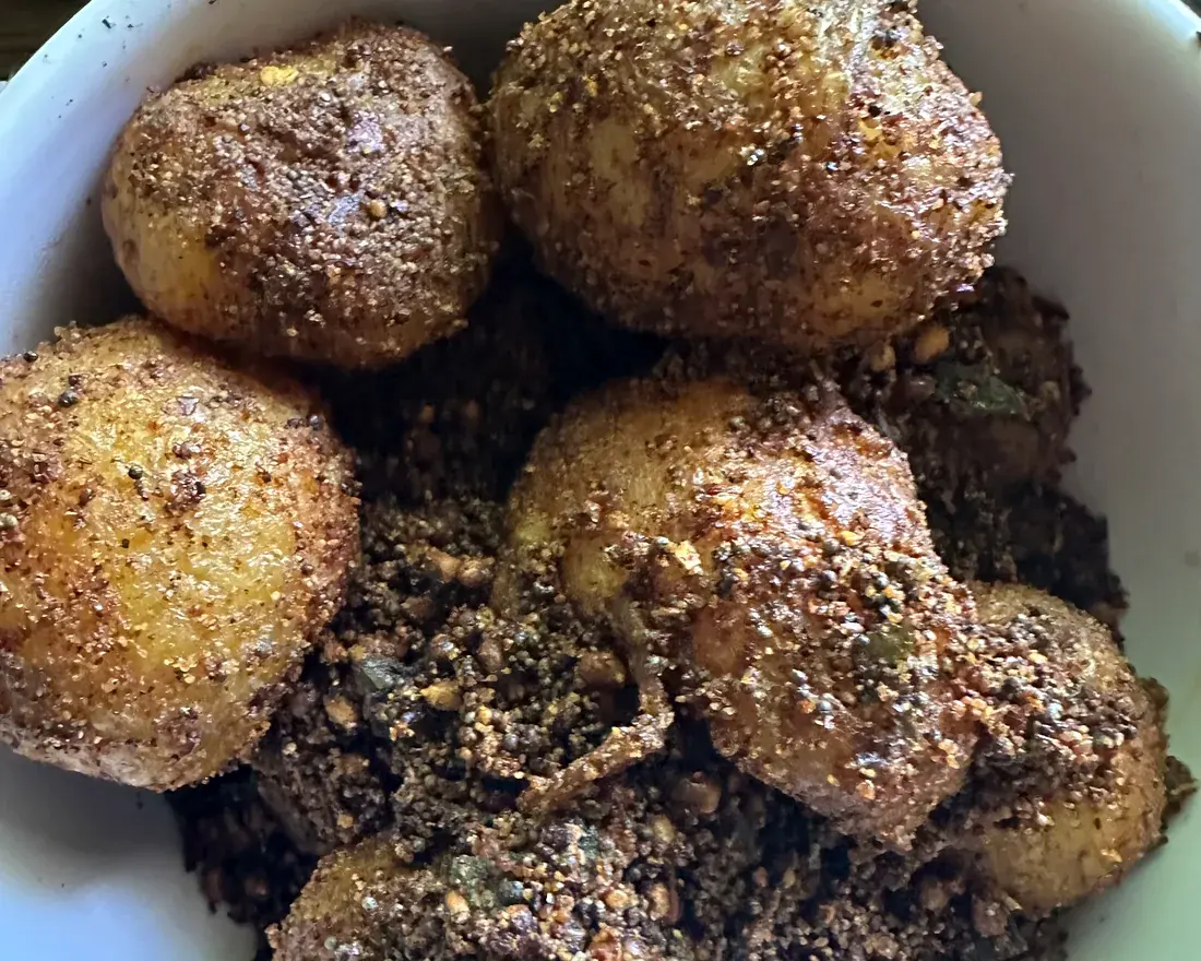 A bowl of baby potatoes tossed in a dark roasted spice crumb with curry leaf